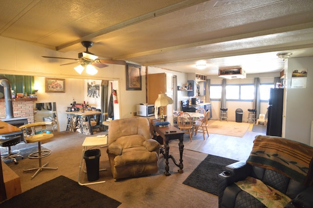 living room featuring ceiling fan, beam ceiling, a textured ceiling, and a wood stove