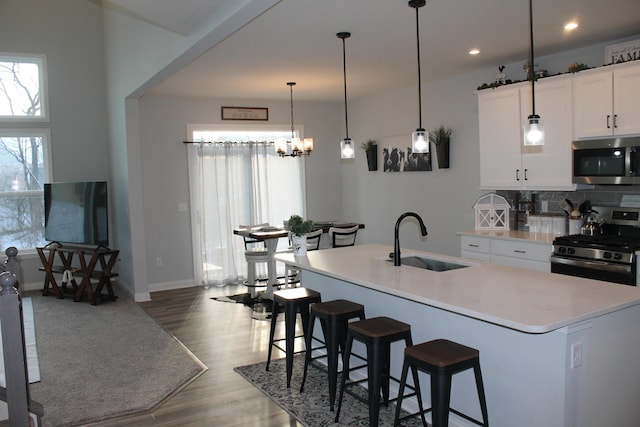 kitchen featuring a center island with sink, stainless steel appliances, hanging light fixtures, white cabinetry, and a sink