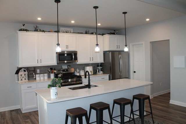 kitchen featuring stainless steel appliances, a sink, hanging light fixtures, light countertops, and an island with sink