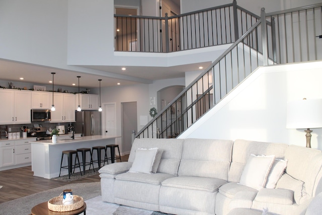 living area with a towering ceiling, stairs, wood finished floors, and recessed lighting