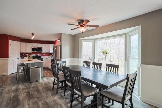 dining space with a wainscoted wall, ceiling fan, and dark wood-style flooring