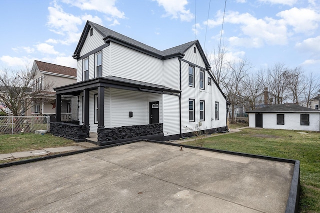 view of side of property with covered porch, a lawn, and fence