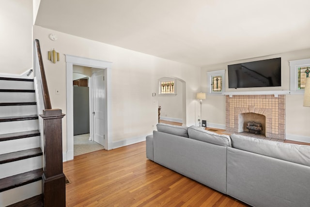 living area featuring arched walkways, stairway, a tiled fireplace, light wood-type flooring, and baseboards