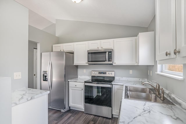 kitchen featuring lofted ceiling, appliances with stainless steel finishes, white cabinets, a sink, and light stone countertops