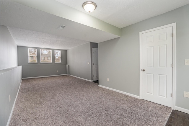 below grade area featuring baseboards, visible vents, dark carpet, and a textured ceiling