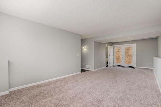 carpeted empty room featuring a textured ceiling, french doors, visible vents, and baseboards