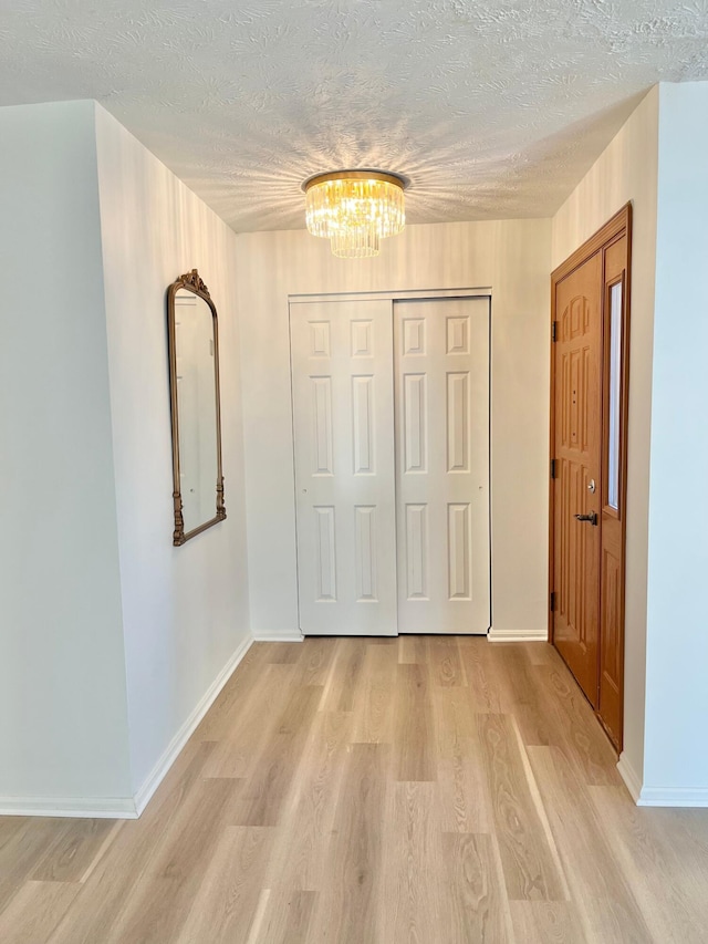 hall featuring light wood-style floors, a textured ceiling, baseboards, and a notable chandelier