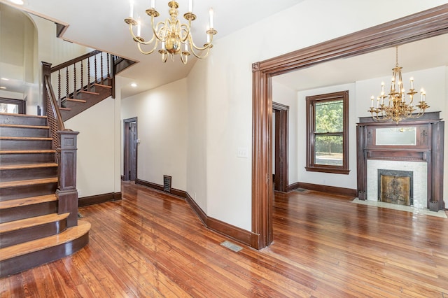 interior space featuring wood-type flooring, visible vents, an inviting chandelier, a fireplace with flush hearth, and baseboards