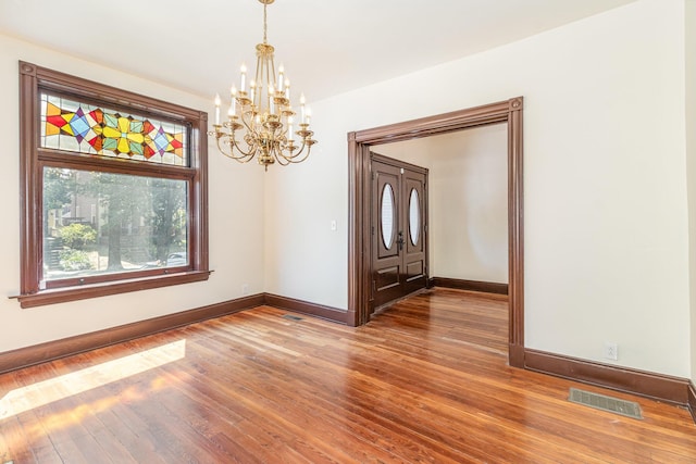 unfurnished room featuring an inviting chandelier, wood finished floors, visible vents, and baseboards