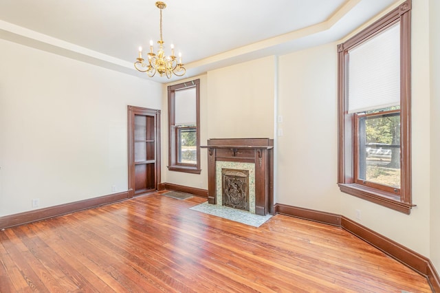 unfurnished living room featuring wood-type flooring, a premium fireplace, baseboards, and a raised ceiling