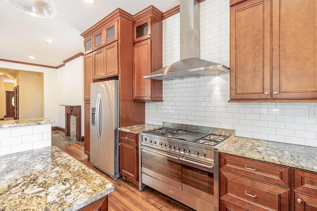 kitchen featuring wall chimney exhaust hood, light wood-type flooring, decorative backsplash, and stainless steel appliances