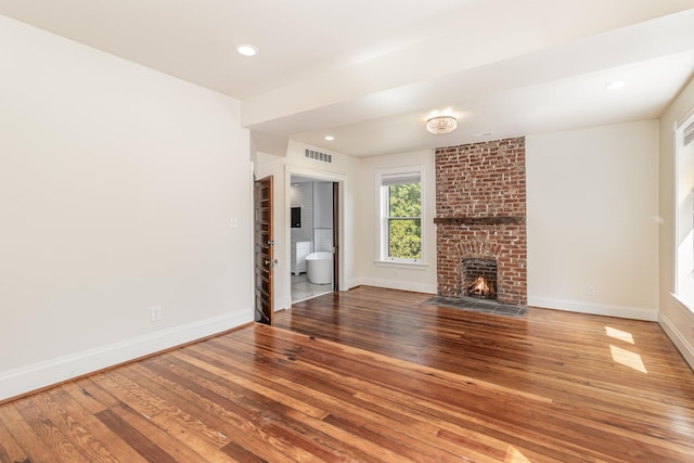 unfurnished living room with baseboards, visible vents, wood finished floors, a brick fireplace, and recessed lighting