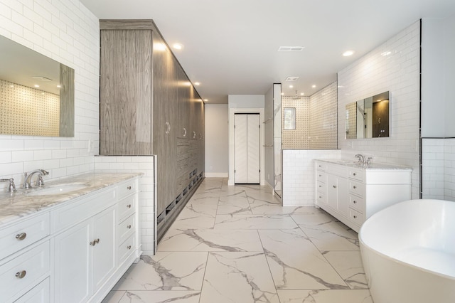 bathroom with marble finish floor, tile walls, a soaking tub, two vanities, and a sink