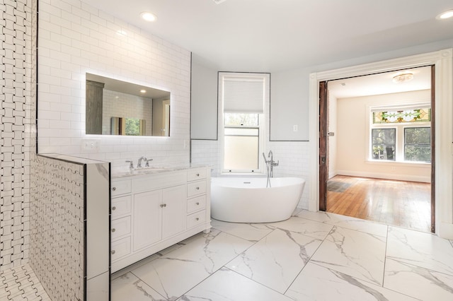 bathroom with marble finish floor, a soaking tub, tile walls, and vanity