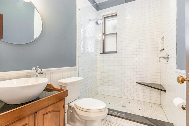 bathroom with wainscoting, a tile shower, vanity, and toilet