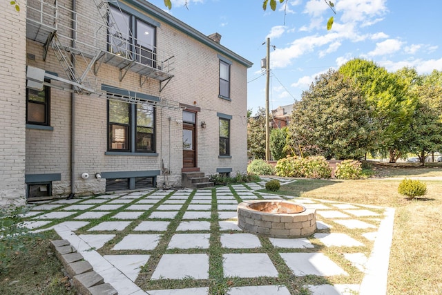 back of house with entry steps, an outdoor fire pit, a patio, a chimney, and brick siding