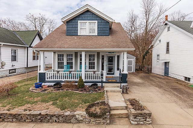 bungalow-style home with fence, a porch, concrete driveway, and roof with shingles