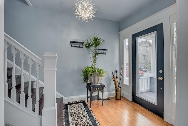 foyer featuring stairs, wood-type flooring, a notable chandelier, and baseboards