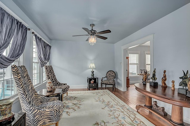 living area featuring wood finished floors, a ceiling fan, and baseboards