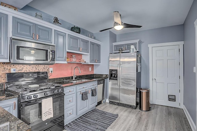kitchen featuring a sink, a ceiling fan, appliances with stainless steel finishes, light wood-type flooring, and dark stone counters