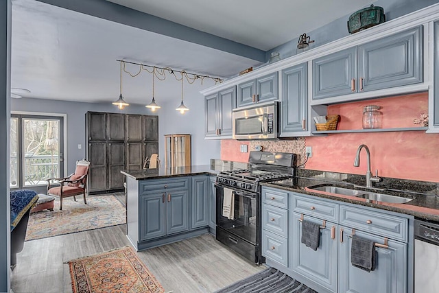 kitchen featuring light wood-style flooring, a peninsula, a sink, appliances with stainless steel finishes, and backsplash