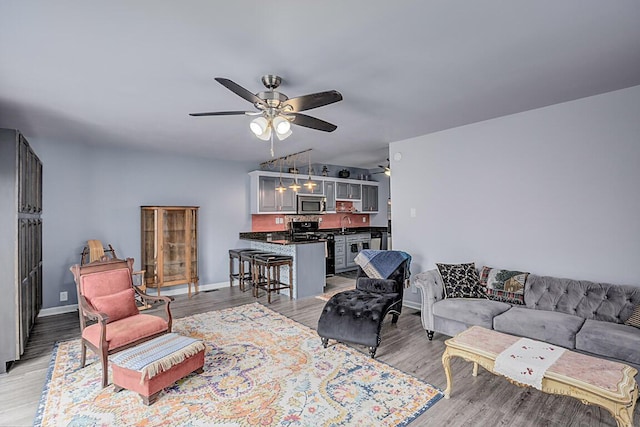 living area with light wood-type flooring, ceiling fan, baseboards, and vaulted ceiling