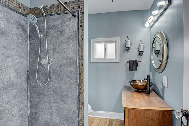 full bathroom featuring baseboards, toilet, wood finished floors, a tile shower, and vanity