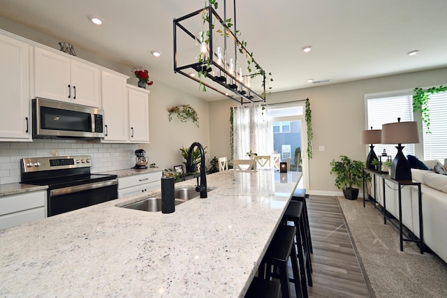 kitchen featuring tasteful backsplash, appliances with stainless steel finishes, hanging light fixtures, white cabinetry, and a sink