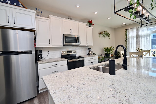 kitchen with tasteful backsplash, appliances with stainless steel finishes, white cabinets, a sink, and light stone countertops