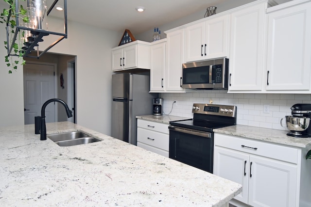 kitchen featuring white cabinets, light stone countertops, stainless steel appliances, and a sink