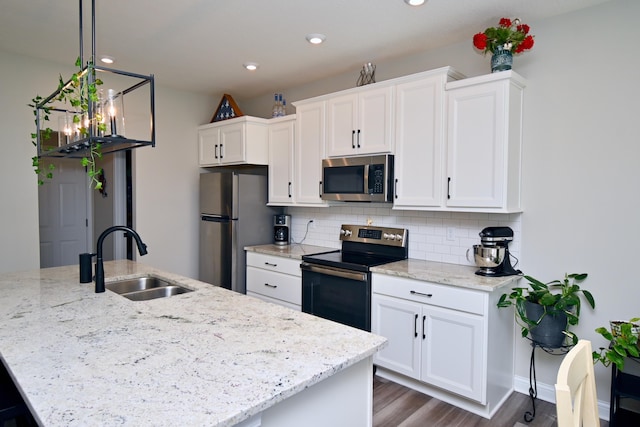 kitchen featuring a kitchen island with sink, stainless steel appliances, a sink, white cabinets, and backsplash