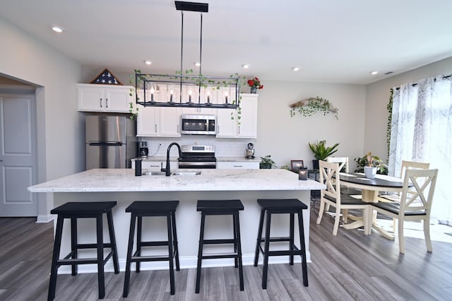 kitchen with a kitchen island with sink, appliances with stainless steel finishes, white cabinetry, and decorative light fixtures