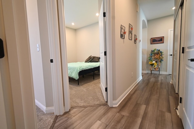 hall featuring baseboards, arched walkways, wood finished floors, and recessed lighting