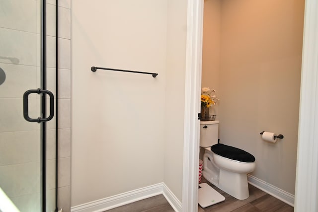 full bathroom with toilet, a shower with door, baseboards, and wood finished floors