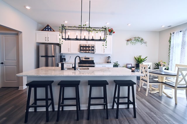 kitchen with appliances with stainless steel finishes, a kitchen island with sink, white cabinetry, pendant lighting, and a sink