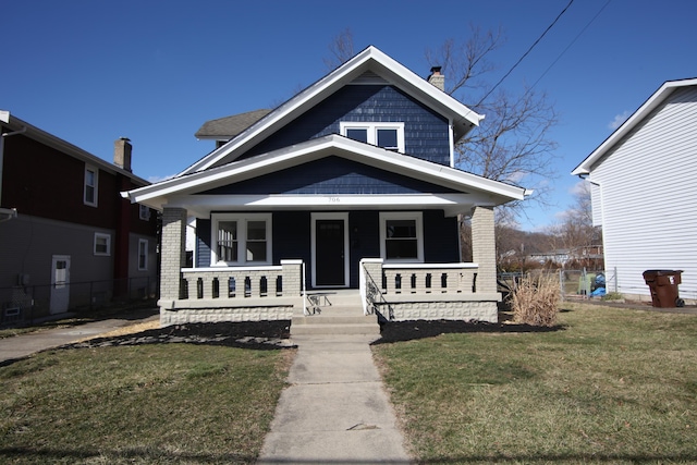 bungalow-style home featuring covered porch, a chimney, brick siding, and a front yard