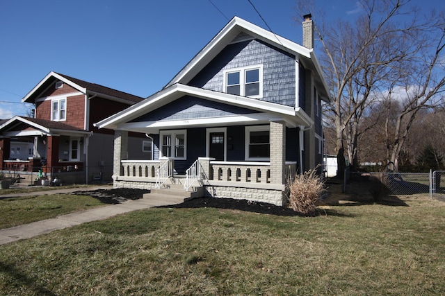 view of front of home with covered porch, brick siding, fence, a front lawn, and a chimney