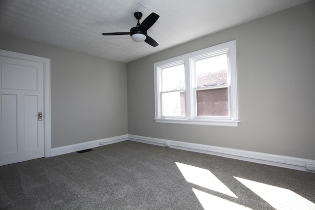 spare room with ceiling fan, baseboards, visible vents, and dark colored carpet