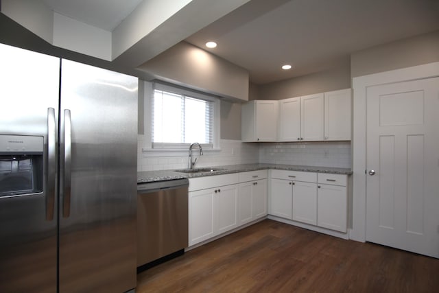 kitchen featuring stainless steel appliances, dark wood-style flooring, a sink, backsplash, and light stone countertops