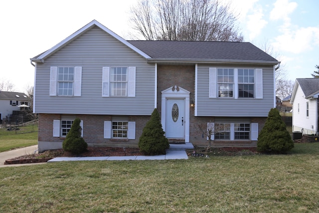 split foyer home with brick siding, central AC unit, a front yard, and a shingled roof