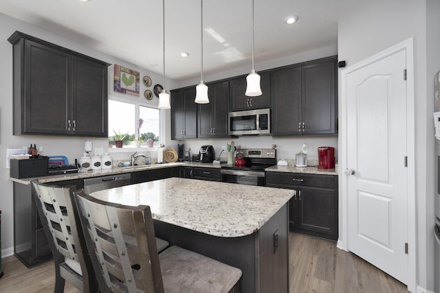 kitchen featuring appliances with stainless steel finishes, light wood-style floors, decorative light fixtures, and a kitchen island