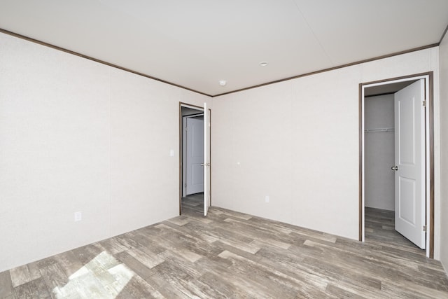 unfurnished bedroom with a closet, a spacious closet, crown molding, and wood finished floors