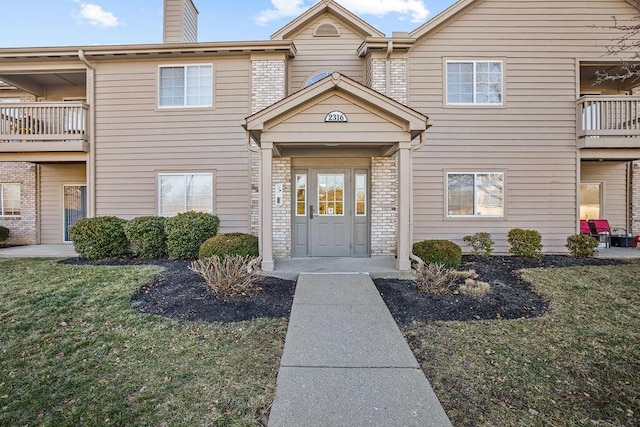 property entrance with a chimney, a lawn, and brick siding