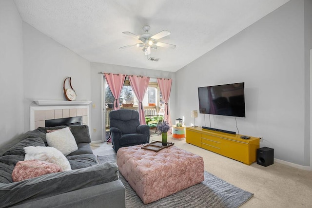 carpeted living area featuring lofted ceiling, ceiling fan, visible vents, baseboards, and a tiled fireplace