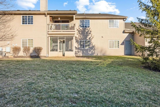 rear view of property featuring a balcony, a chimney, central AC unit, and a lawn