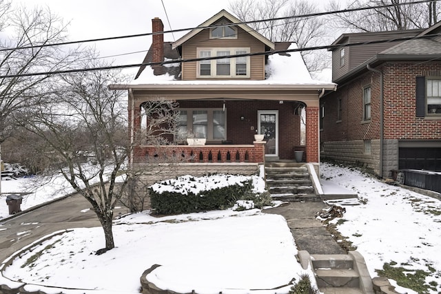 view of front facade featuring covered porch, brick siding, and a chimney