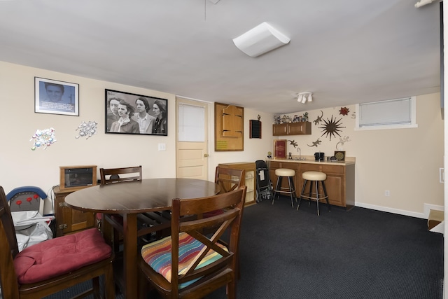 dining room featuring dark colored carpet, baseboards, and wet bar