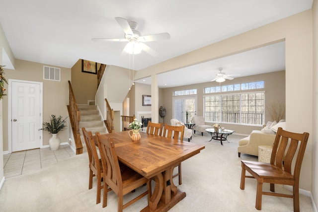 dining area with light carpet, baseboards, visible vents, stairway, and ceiling fan