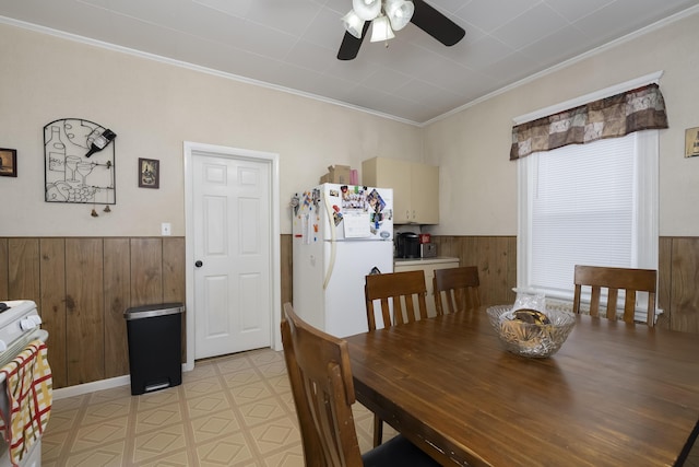 dining room with ornamental molding, a wainscoted wall, wood walls, and light floors