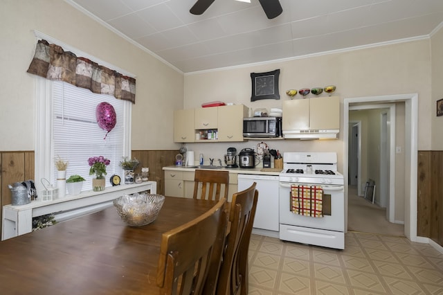 dining space with wooden walls, a ceiling fan, wainscoting, crown molding, and light floors